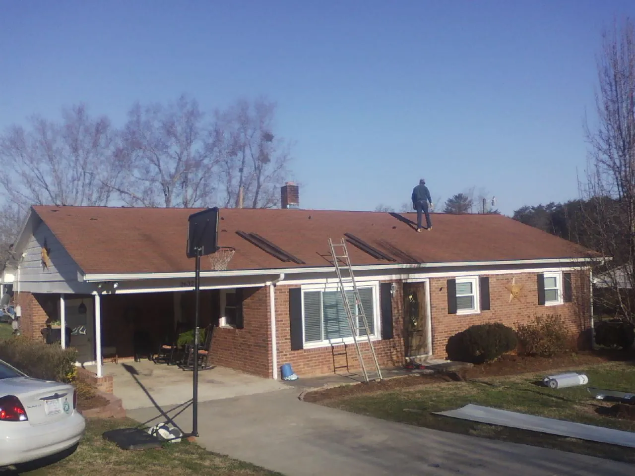 Roofer stripping a shingle roof on a brick ranch before metal panels in Fair Bluff