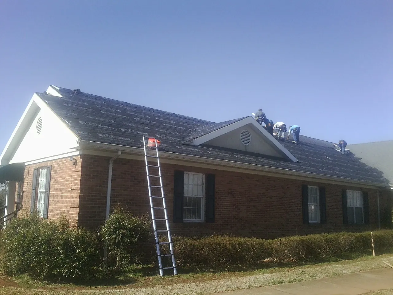 Crew tearing shingles off a brick ranch roof with a ladder set — Metal Roof Repair work by our crew in Fair Bluff