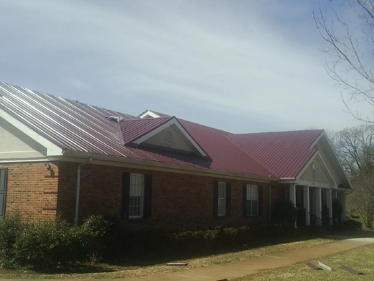 Red metal roof with gabled entries on a long brick building, from a Hail Damage Roof Repair job in Fair Bluff