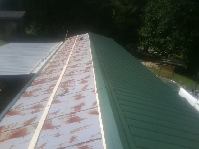 Old rusted panels beside newly installed green metal roofing — Wind Damage Roof Repair by Roofing Brothers in Fair Bluff