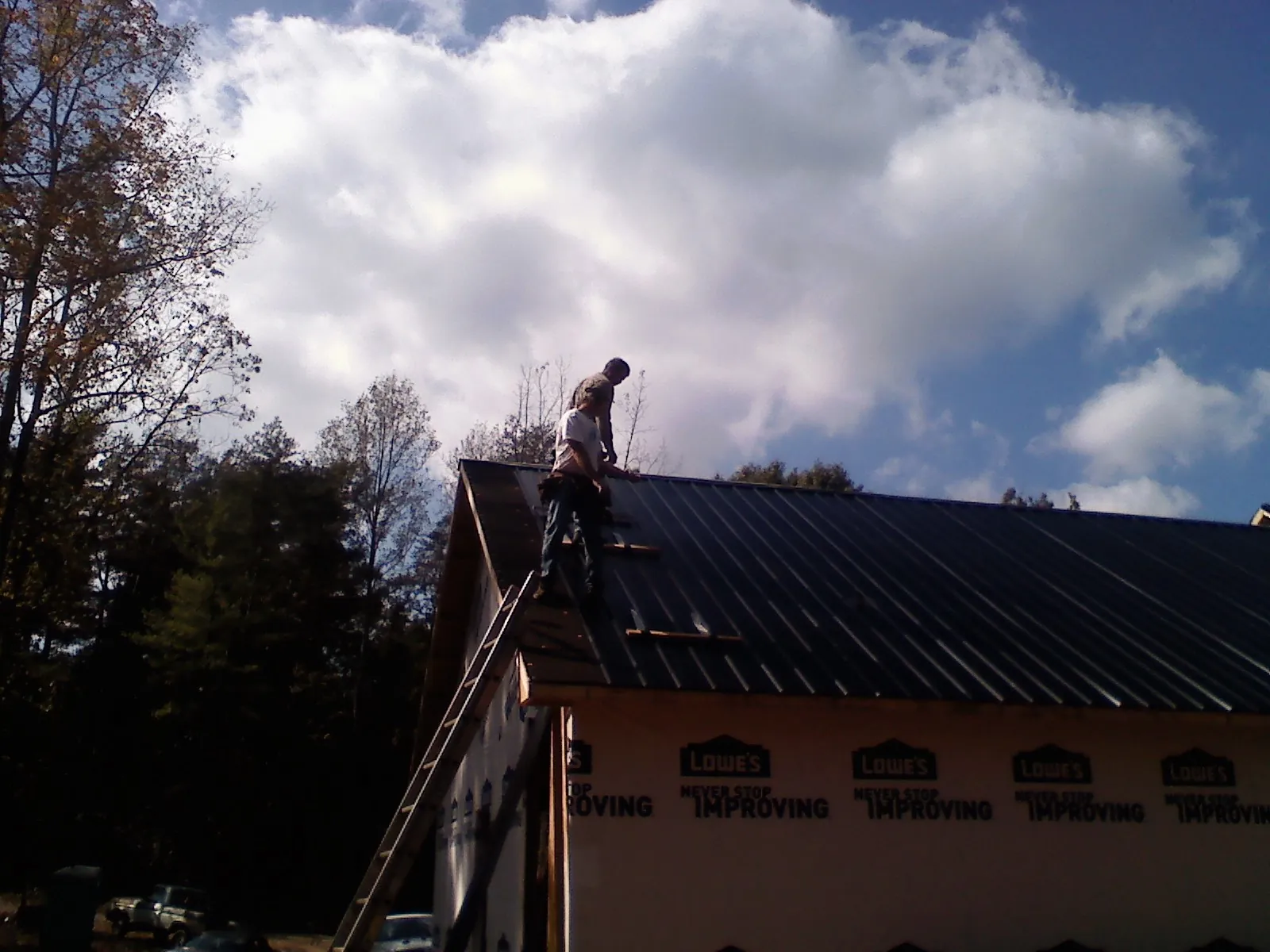 Roofer fastening dark metal panels high against a cloudy sky, from a Roof Inspection job in Fair Bluff
